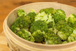 Close up of steamed broccoli in a bamboo pan.
