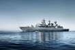 Large grey modern warship sailing in still water. Clear blue sky. Baltic sea, Germany. Global communications, international security theme. Panoramic image