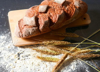 rustic crusty bread and wheat ears on a dark wooden table