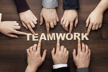 Teamwork concept. Different hands of men and women connect letters into one word on the brown wooden table background. Each has its own role in team