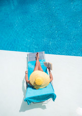 Wall Mural - Woman relaxing at the swimming  pool reading a book