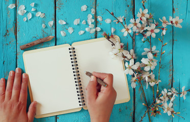 Wall Mural - woman writing on blank notebook next to spring white cherry blossoms tree on vintage wooden table. 