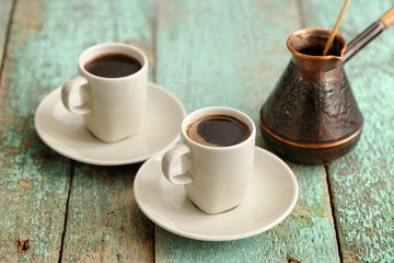 Two cups of fresh black coffee and copper cezve on old wooden ta