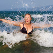© Veresovich - Young woman enjoying a dip in the sea on a background of foam and spray. Girl and sea wave. Bright sunny day. Selective focus.