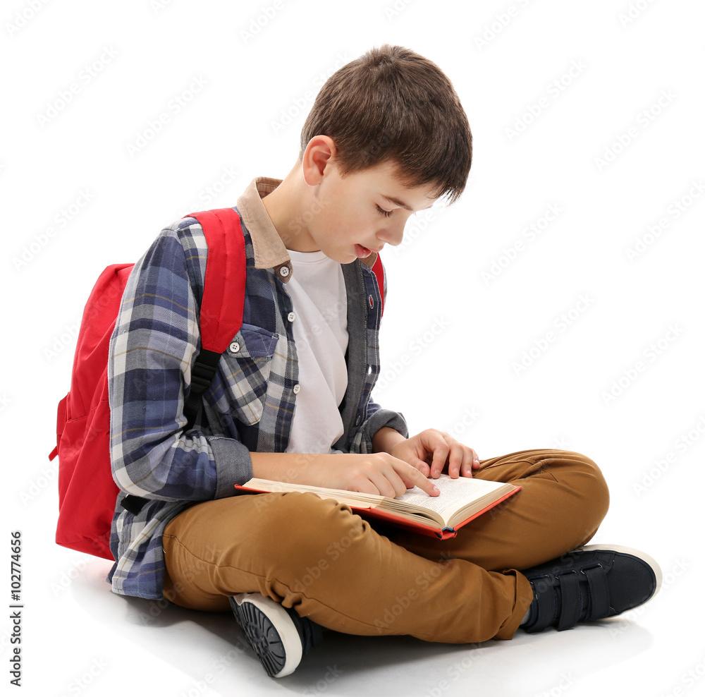 Cute little boy with red backpack reading a book, isolated on white
