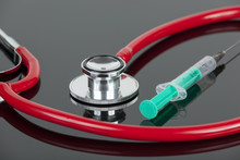 Red Stethoscope And Green Hypodermic Needle On Lab Worktop