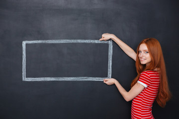 Happy woman holding drawn frame over chalkboard background