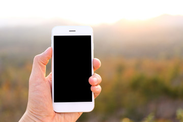 hand holding mockup smartphone with sunlight and mountain backgr