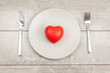 red heart on a plate, fork and knife on a wood background
