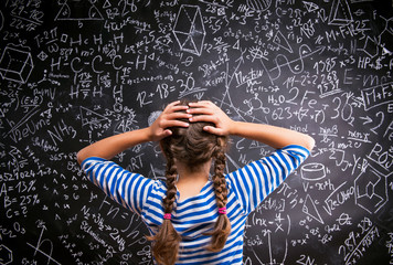 thinking girl holding head against big blackboard, back view
