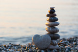 Fototapeta Desenie - Grey stone in shape of heart in front of balanced stones on still water background