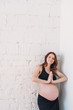 © lumenphotos - Pregnant woman with red hair in black clothes on a white wall