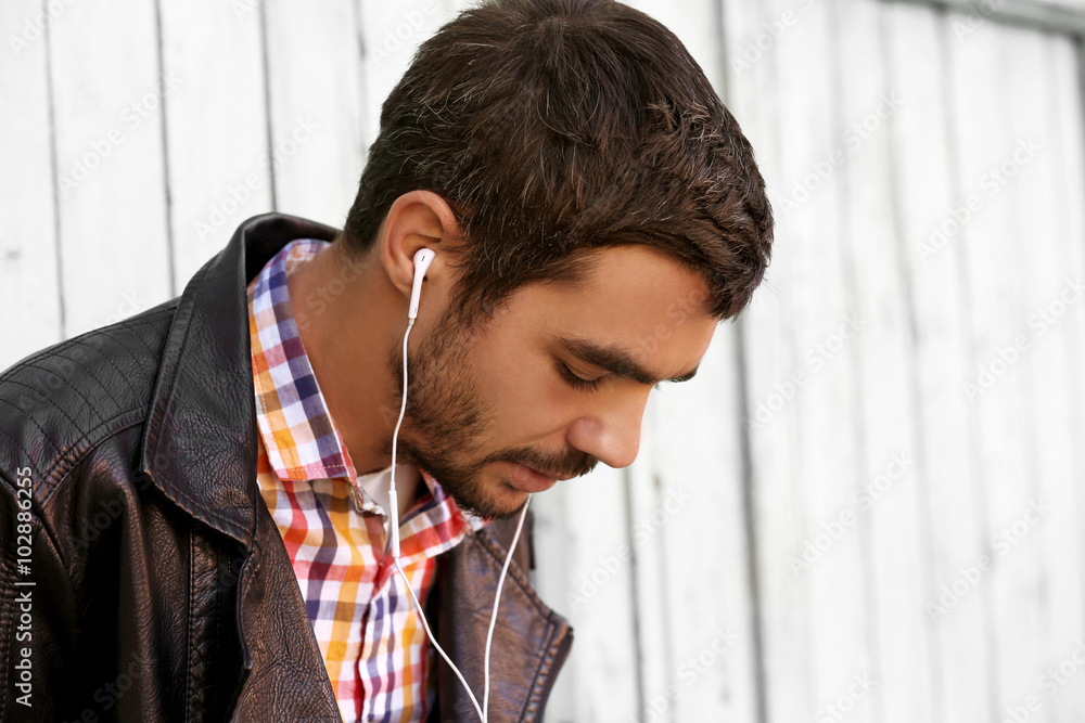 Young man listening to music on a house wall background