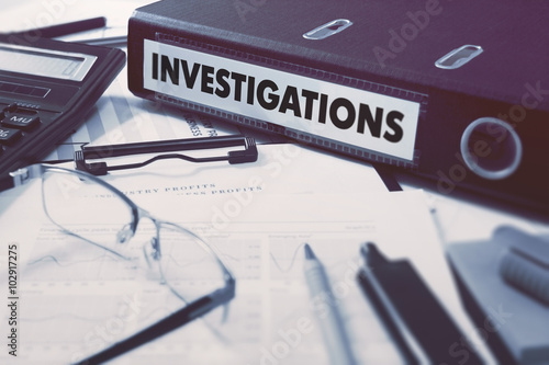 Fotografía Ring Binder with inscription Investigations on Background of Working Table with Office Supplies, Glasses, Reports
