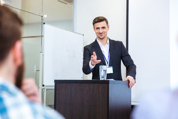 Poster - Smiling businessman standing at tribune in conference hall