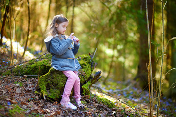 adorable little girl picking the first flowers of spring in the woods