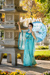 beautiful geisha with a blue umbrella near stone pagoda on background of blur fountain