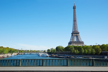 Eiffel tower and empty sidewalk bridge on Seine river, clear blue sky