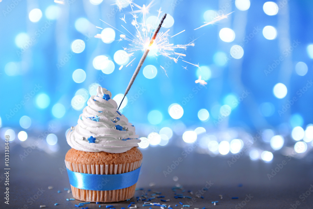 Cupcake with white cream icing and sparkler on a glitter background