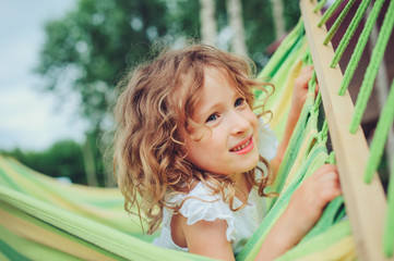 happy child girl relaxing in hammock on summer camp in forest. Outdoor seasonal activities for kids.