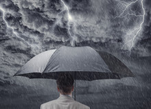 Businessman With Umbrella Sheltering From Approaching Storm
