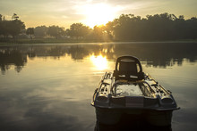 Small Empty Fishing Boat On Lake River Water Pond At Sunrise Sunset Dawn Early Morning Dusk With Sun Rays And Trees Forest On Horizon Feeling Peaceful Relaxed Serene Calm Meditative
