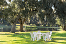 White Plastic Table And Chairs Outside In A Garden On Green Lawn By A Pond Or Lake In The Afternoon Sun And A Peaceful Relaxing Serene Tranquil Setting