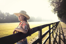 Cowgirl Woman In Cowboy Hat Flannel Shirt And Jeans Leaning On Country Rural Fence Looking Confident Happy Serene Smart Alone Waiting Watching Patient