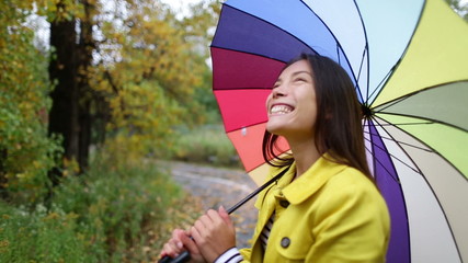 Wall Mural - Fall / Autumn concept - woman excited under rain with umbrella. Beautiful young female wearing raincoat surprised and excited in the rain. Mixed race Asian Caucasian girl in her 20s walking in forest.