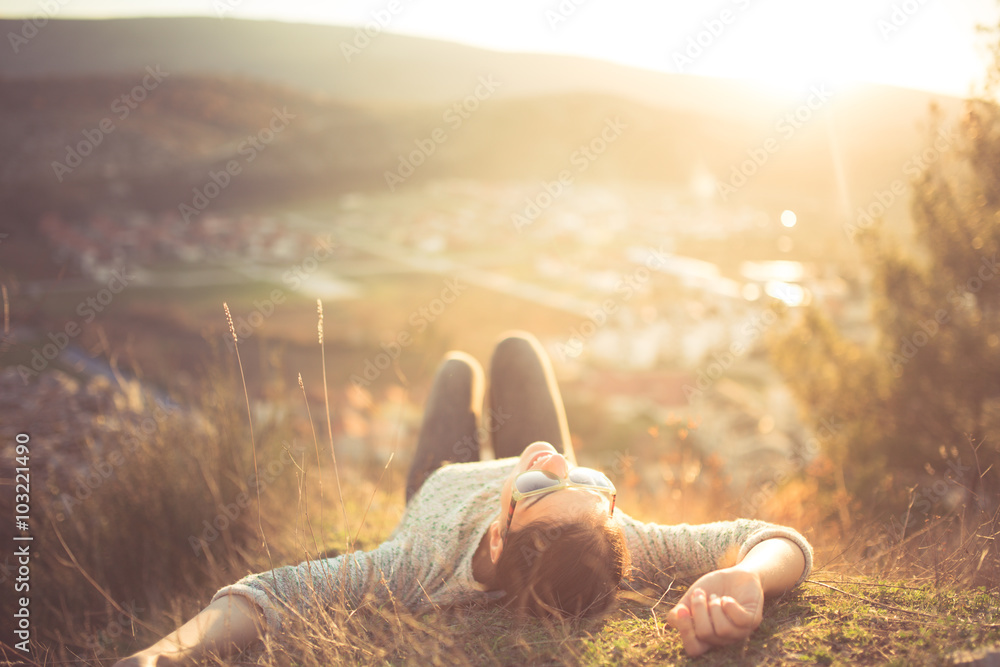 arefree happy woman lying on green grass meadow on top of mountain edge cliff enjoying sun on her face.Enjoying nature sunset.Freedom.Enjoyment.Relaxing in mountains at sunrise.Sunshine.Daydreaming