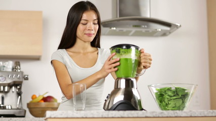 Wall Mural - Woman making, pouring, drinking green vegetable smoothie with blender. Healthy eating lifestyle with young woman preparing blending smooithies drink with spinach, carrots, celery at home in kitchen.