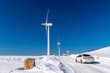 Wind Turbine And Car With Blue Sky In Winter Landscape.