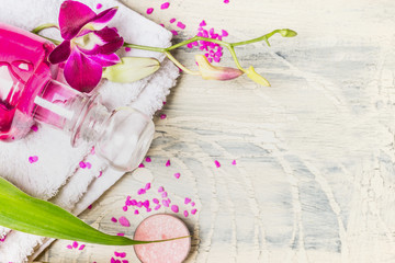 Wall Mural - Close up of glass bottle of lotion with pink orchid flowers  on white towel on light wooden background, top view, place for text. Spa, wellness or body care concept