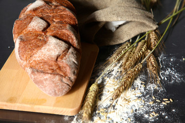 rustic crusty bread and wheat ears on a dark wooden table