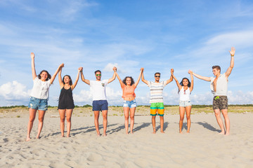 Multiracial group of friends with raised hands on the beach