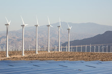 Solar Energy Windmills And Solar Panels In California. Solar Panels Energy In A California Desert With Mountains In The Background. Sunlight, Solar Panels And Wind Turbines. 