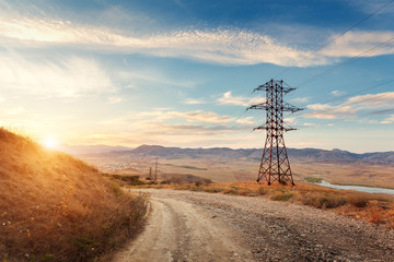 High voltage tower in mountains on the background of colorful sky at sunset.  Electricity pylon system. Summer evening. Industrial landscape 