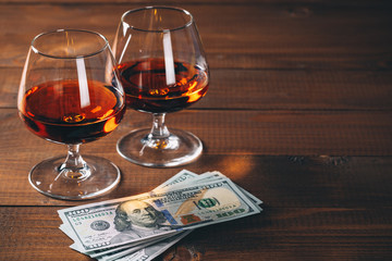 Two glasses of cognac with wad of money on the wooden table.