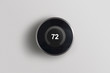 © wmarkusen - A simplistic photo of a round, modern, programmable digital thermostat, on a clean white wall.