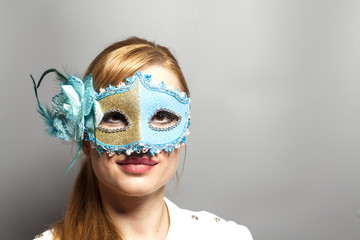 Beautiful young woman in mysterious venetian mask on gray backgr