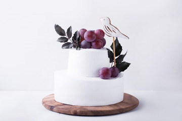 White two-tiered cake decorated with a bird grapes and leaves on a light background