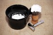 Shaving brush with foam, razor and mug on a burlap background, retro effect