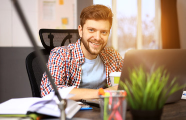 Canvas Print - Enjoying good working day. Confident young man working on laptop while sitting at his working place