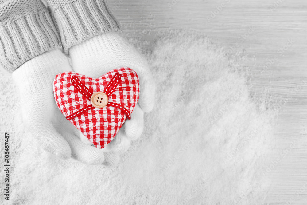 Hands in warm white gloves holding red heart on snowy background