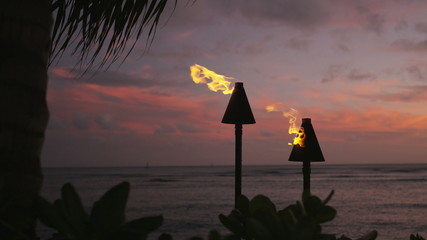 Wall Mural - Torches with fire and flames burning in Hawaii sunset sky by palm trees. Beautiful slow motion torches on Hawaiian Waikiki beach, Oahu. RED EPIC SLOW MOTION