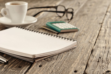 open notepad with pen, cup of coffee, calculator and glasses