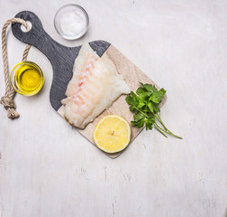 Raw fish fillet on a cutting board with lemon, herbs, butter and salt border ,place for text on wooden rustic background top view close up