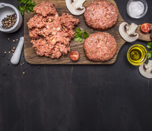 Two Cutlets For Burgers With Minced Meat On A Cutting Board With Herbs, Butter And Salt Border ,place For Text On Wooden Rustic Background Top View Close Up