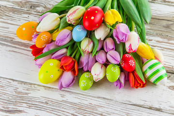  Colorful tulips with easter eggs on wooden table.