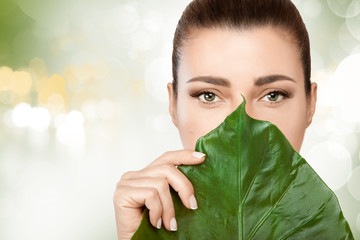 Wall Mural - gorgeous young woman with a fresh leaf to her face